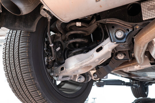 Car rear axel assembly with control arm, coil spring and shock absorber. Wide angle, looking up shot of a lifted car in a repair shot, no people