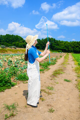 高原で虫取り網を持つ麦わら帽子の女の子　夏の自然体験