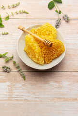 Honeycomb in bowl with honey dipper and fresh mint on wooden table