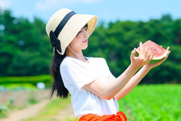 夏の高原で麦わら帽子をかぶった小学生の女の子がスイカを持つ風景