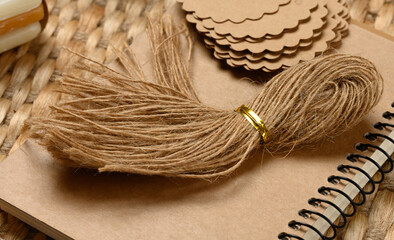 Bundle of natural jute twine on a spiral bound notebook. Various craft supplies are in the background