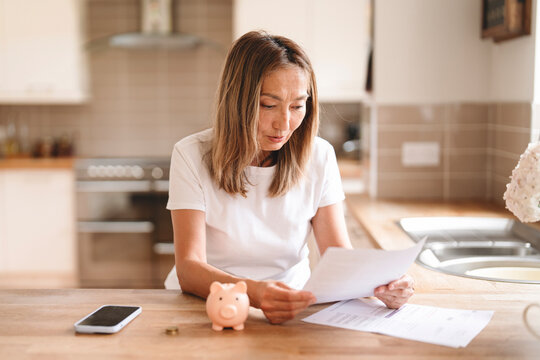 Woman reviewing bills at home in a modern kitchen while managing finances with a piggy bank nearby