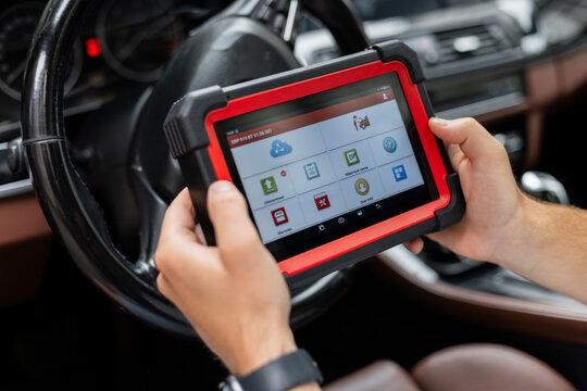 Automotive technician performing computer diagnostics with handheld device. mechanic holds a modern diagnostic scanner inside a car, checking vehicle systems and electronics. Automotive technology