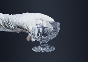 A Detailed Close-up of a Hand Wearing a Pristine White Rubber Glove Delicately Holding a Clear, Ornate Glass Cup