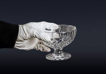A Detailed Close-up of a Hand Wearing a Pristine White Rubber Glove Delicately Holding a Clear, Ornate Glass Cup