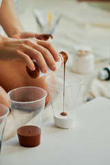 Vertical shot of unrecognizable woman wearing white shirt sitting on floor in studio pouring acrylic paints into plastic cups