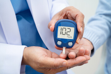 Asian doctor using digital glucose meter for check sample blood sugar level to treatment diabetes.
