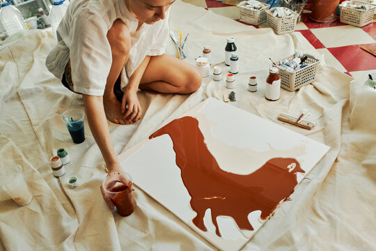 Horizontal high angle view shot of modern artist creating fluid art picture adding brown acrylic paint