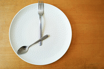 Intermittent fasting concept: empty white plate with fork and spoon positioned like clock hands at 8 o'clock. Time-restricted eating and meal timing for circadian rhythm diet. Fasting window concept