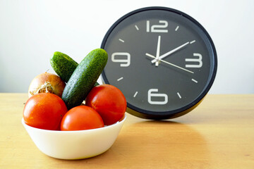 Fresh vegetables in white bowl next to modern clock symbolizing efficient meal planning and time management. Concept of productivity, wellness routines, sustainable lifestyle, healthy eating habits