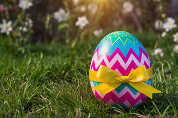 Colorful Easter egg with yellow ribbon on grass flowers