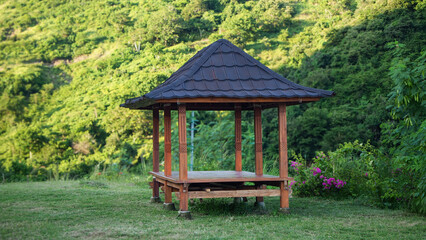 traditional wooden gazebo stand in field with green background surrounded by grass, scenic tropical view, ideal for nature, travel, and outdoor photography themes.