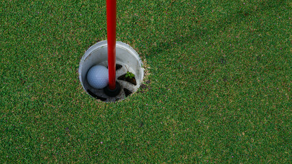 Golf ball in hole on a green lawn in a beautiful golf course with morning sunshine.