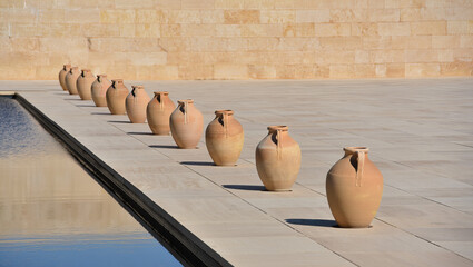 Terracotta amphorae lined up by modern water feature
