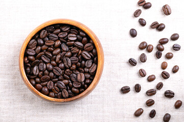 Roasted  Arabica coffee beans, in a wooden bowl, on linen. Dark brown roasted seeds of berries from Coffea arabica, also known as Arabian, mountain or Arabica coffee. Close-up, from above. Food photo.