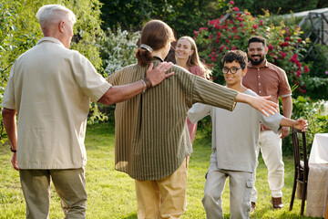 Multiethnic family group including senior Caucasian man, middle aged Caucasian woman, young adult Caucasian woman, young adult Middle Eastern man, preteen boy greeting each other outdoors