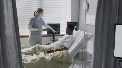 Female medical worker in scrubs and face mask explaining vital signs on patients bedside monitor during checkup in hospital - Powered by Adobe