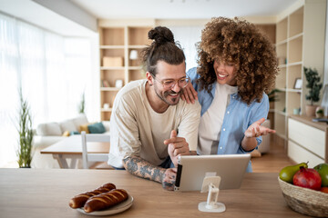 Happy couple using digital tablet in modern kitchen, enjoying breakfast and online content