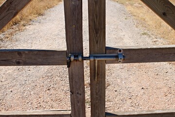 Close-up of a wooden fence gate with metal bolt and padlock in a rural field in Spain. The weathered wood texture, warm sunlight and dry countryside
