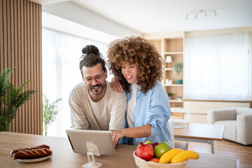 Happy couple using digital tablet in modern kitchen