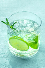 Gin tonic, a glass of gin with soda, lime, rosemary, and ice, on a blue background, fresh summer cocktail