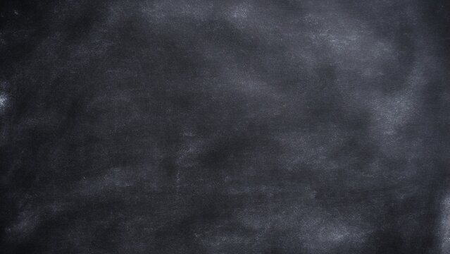 Black chalkboard texture with rubbed chalk. White chalk dust on a black chalkboard. Chalk smudges on dark blackboard. Empty classroom blackboard background with space for design.