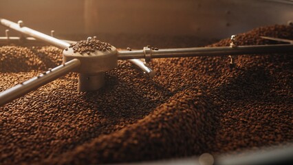 Coffee beans rotating inside cooling tray under moving metal arms of industrial roasting machine....