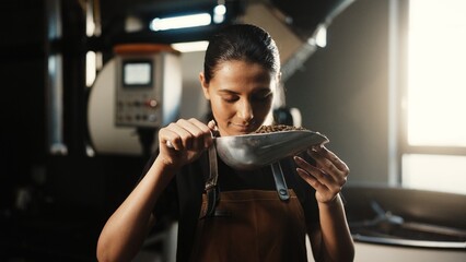 Smiling Caucasian woman in brown apron holding metal scoop filled with roasted coffee beans....