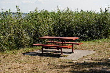 Obraz premium Picnic Area: A red picnic table stands on a concrete pad near a lush green treeline and lake.