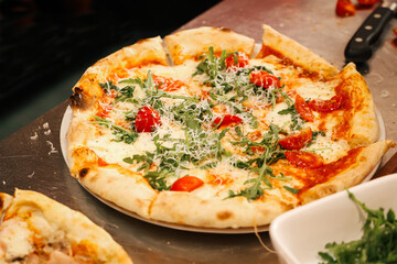 Freshly baked Italian pizza with mozzarella, arugula, and cherry tomatoes served on a plate in a professional kitchen, authentic food preparation