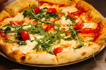Fresh Italian pizza with melted mozzarella, arugula, and cherry tomatoes on a plate, authentic Mediterranean cuisine in a restaurant kitchen