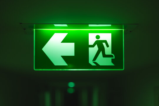 Exit way arrow direction guidance sign green color light emergency exit sign in a dark room