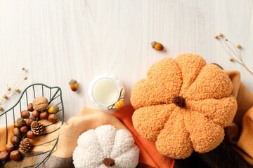 Autumn flat lay with plush pumpkins, candle, nuts, pinecones, and leaf-shaped basket on wooden surface.