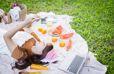 Woman enjoys leisure picnic on blanket with fresh fruit and laptop nearby while people concept of family relaxation and outdoor enjoyment creates peaceful atmosphere