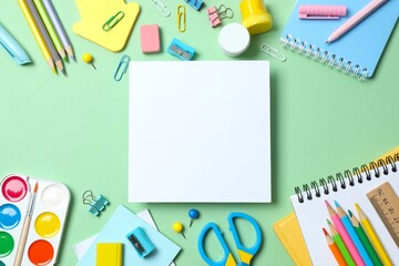 White paper card with school supplies including notebook, pencils and stationery on green background