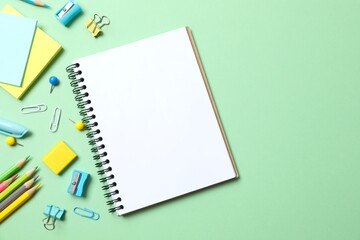 School supplies including notebook, pencils and stationery on green background, top view
