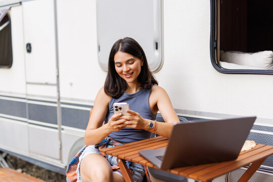 Young woman behind laptop with phone working near trailer.