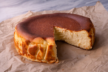 Whole baked cheesecake with one slice cut out, placed on brown parchment paper over marble table, showing creamy interior, golden crust, and rustic homemade dessert presentation