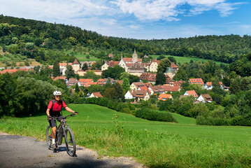 Fototapeta premium nice senior woman riding her electric mountain bike in the Schoenbuch Forest in front of Bebenhausen Monastery near Tuebingen in Baden-Württemberg. Germany 