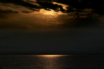 Sun shining through dark clouds over calm water reflecting its light