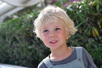 Little blond boy portrait outdoors in summer greenery