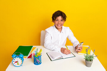 Smiling boy studying at a bright desk with school supplies and a vibrant yellow background for an academic theme