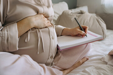 Pregnant woman writing in notebook preparing for maternity hospital
