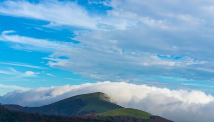 A vibrant sky with wispy clouds above a hilltop shrouded in a blanket of white clouds.