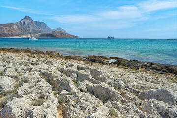Scenic landscape of the Mediterranean sea on Crete, Greece. Rocks, lonely sailboat, mountains in the background and blue, clear sky.	  