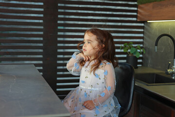 Cute little girl sitting at kitchen counter in modern home interior. High quality photo