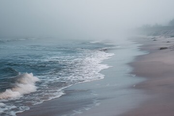 Fototapeta premium Moody foggy beach with muted blue and gray tones, tranquil mysterious coastline for creative projects, relaxation advertising, travel content, atmospheric backdrop