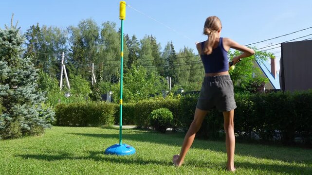 Child joyfully plays tetherball in vibrant green yard on sunny summer day, showcasing skill and energy