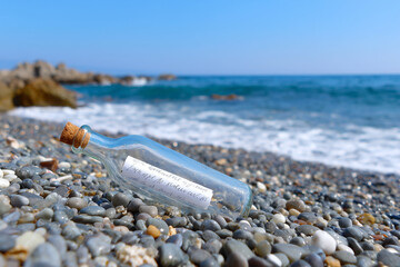 Message in a bottle resting on a pebble beach, near the calm sea