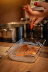 Female hand sprinkles spices on grilled salmon in a cast glass grilling pan. Stir fried salmon in the pan.